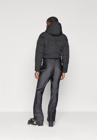 Must must jakker kapuutsiga, ribakäistega ja tikandiga, koos siledate mustade pükstega ja mustade nööbisaabastega.