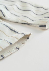 Kremowa tkanina z falistymi niebieskimi i beżowymi paskami; posiada mankietowane wykończenie i miękką fakturę, odpowiednia do casualowego noszenia lub warstwowego ubierania się.