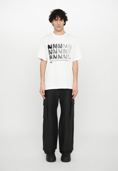 T-shirt bianco a maniche corte con un motivo grafico nero; abbinato a pantaloni cargo neri a vestibilità ampia e scarpe slip-on nere.