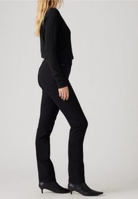 Jeans ajustados negros con una textura suave y ligera elasticidad, combinados con un top negro de manga larga. Los accesorios incluyen tacones negros puntiagudos.