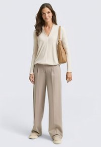 Bež rebrasti džemper s V izrezom, u kombinaciji s bež hlačama širokih nogavica. Dodaci uključuju smeđu torbu preko ramena i krem platnene cipele na platformu.