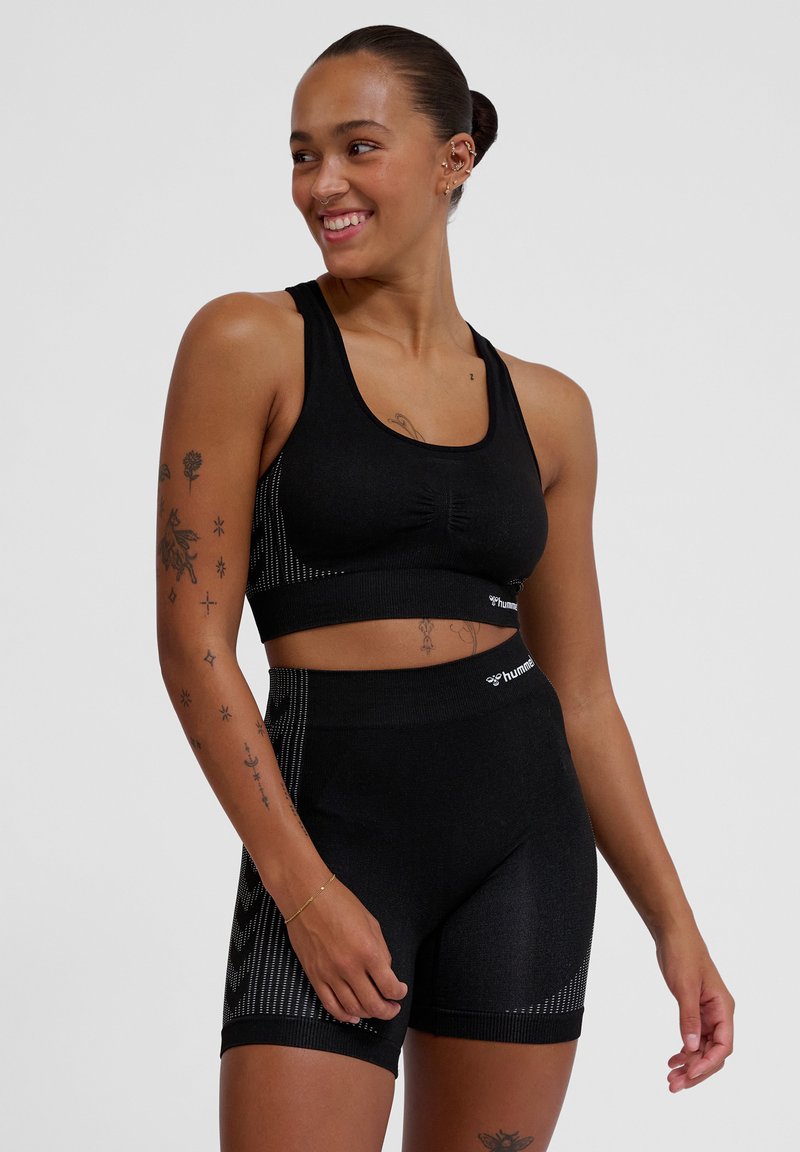 Svart atletisk crop-top med en bred kant och subtil textur, kombinerad med högmidjade svarta shorts med vertikala ränder och logotypdetaljer.