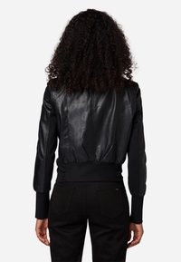 Giubbotto bomber in pelle nera con polsini e vita a coste aderenti. Presenta una texture liscia con cuciture verticali, abbinato a pantaloni neri.