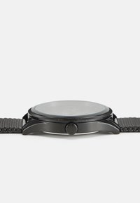 Black metal wristwatch with a smooth round dial, textured bezel, and a mesh band. Features a prominent crown on the side for adjusting time.