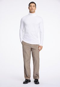 Balta ilgomis rankovėmis golfas, derinamas su smėlio spalvos aksominio audinio kelnėmis ir juodais batais. Apranga pasižymi siauru kirpimu ir tekstūruota medžiaga.