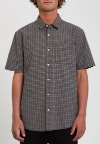 Chemise à manches courtes à boutons, à carreaux noir et blanc, avec une poche appliquée et une petite étiquette logo sur la partie gauche de la poitrine.