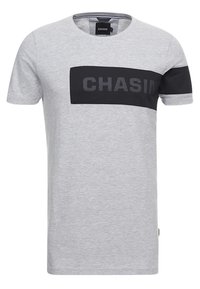 Světle šedé tričko s krátkým rukávem a černým vodorovným pruhem přes hrudník a levý rukáv, s nápisem "CHASIN" vytištěným tmavými písmeny.