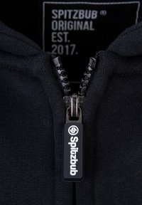 Zwarte zip-up hoodie met een gladde rits en gemerkte trekker. Het label toont "SPITZBUB ORIGINAL EST. 2017" in witte tekst op een donkere achtergrond.