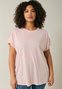 Ljusrosa kortärmad topp i mjukt material med spetsdetaljer vid axlarna och en avslappnad passform. Rundad nederkant och rundad halsringning.