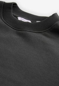 Sudadera de color gris oscuro con un cuello de tripa acanalado y una textura suave. La tela es blanda, con costuras mínimas visibles en los bordes.