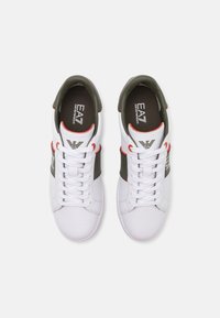 Hvite sneakers med en glatt lærfinish. Har grå detaljer og røde innslag. Snøring med strukturert såle og logo.