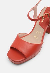 Sandales à talons en cuir rouge avec une large bride à l'avant, une boucle à la cheville et une semelle intérieure Texturée. Bout carré et semelle intérieure rembourrée.