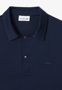 Marinblå polo tröja i bomull, med ribbad krage, knappslå och en broderad logotyp på vänster bröst. Klassisk passform.