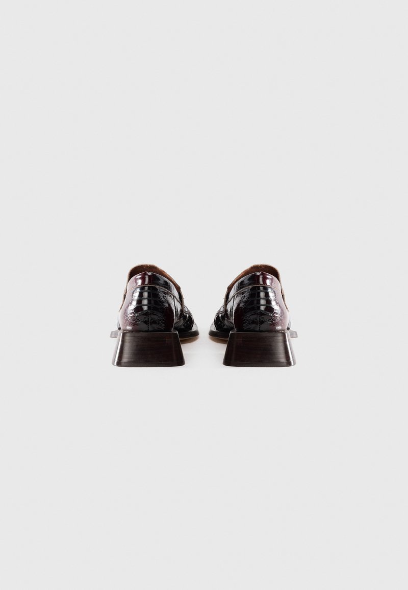 Une paire de chaussures de ville en cuir verni bordeaux foncé avec de petits talons carrés, vue de l'arrière sur un fond blanc uni.