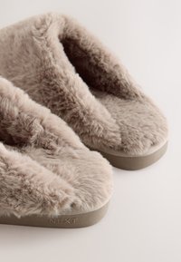 Pantofole pelose in beige chiaro con tomaia in pelliccia, design con punta aperta e suola in gomma resistente. Caratterizzate dal logo impresso sul lato.