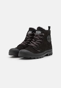 Black high-top boots made of suede, featuring a textured rubber sole, grey laces, and a circular logo accent on the side.