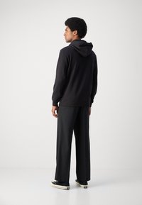 Sweatshirt à capuche noir avec une coupe décontractée et des poignets côtelés, associé à un pantalon noir ample et des baskets noires décontractées.