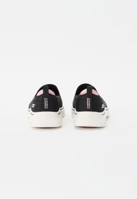 Sapatilhas atléticas pretas de slip-on com um upper respirável, sola branca e detalhes em rosa no calcanhar. Apresenta logotipo na parte traseira.