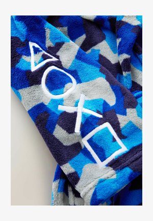 Minkštas mėlynas ir pilkas kamufliažo rašto pledas, papuoštas baltais siuvinėtai trikampiais, apskritimais ir kvadratais. Minkšta tekstūra.