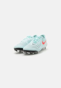 Bleg blå fodboldstøvler med tekstureret overdel, sorte og hvide stød, og pink Nike-logo. Har et strømlinet design og snørebåndslukning.