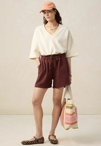 Top oversized blanc à col en V, short marron avec une taille élastique, ballerines imprimé léopard et un sac fourre-tout rayé avec deux poignées.