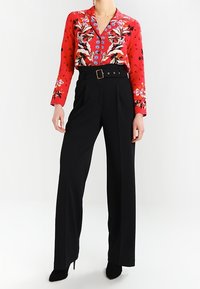Red floral blouse with long sleeves and collar, paired with high-waisted black trousers featuring a belt and buckle detail.