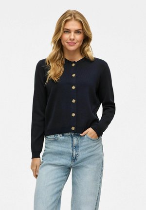 Donkerblauwe gebreide cardigan met een ronde halslijn, knoopsluiting en lange mouwen, gepresenteerd met lichtblauwe jeans.