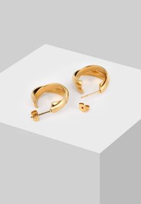 Ein Paar glänzende goldene Creolen mit offenen Enden und Schmetterlingsverschlüssen, präsentiert auf einer weißen geometrischen Fläche.