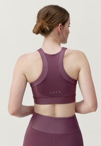Burgundy sportbh med en figursyd design, racerback-stil och subtila reflektordetaljer på baksidan, tillverkad av ett smidigt, elastiskt material.