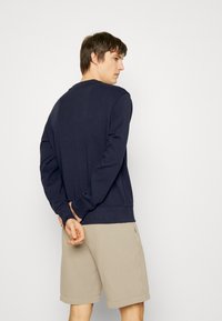 Sweatshirt azul-marinho com mangas longas, decote redondo e bainha canelada, combinado com calções bejes. Design simples, tecido macio e ajuste descontraído.