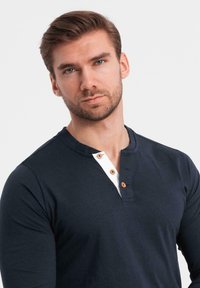 Marineblaues Langarm-Henley-Shirt mit einer weißen Knopfleiste und zwei Holzknöpfen, weicher Textur und taillierter Passform.