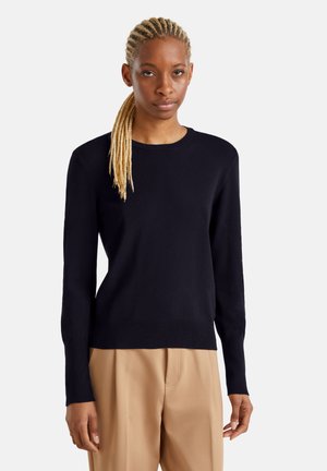 Pull en tricot noir à manches longues et col rond. Texture douce, cintré à la taille, associé à un pantalon beige.