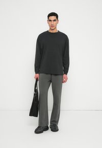 Maglietta nera a maniche lunghe con scollo rotondo, pantaloni grigi a zampa d'elefante, calzature nere e borsa tote nera. Tessuto morbido, design minimalista.