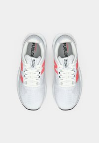 Baskets de sport blanches avec une tige texturée, présentant des accents roses et des lacets blancs. Comprend une semelle intérieure grise et un logo sur la languette.