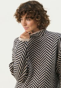 Sweter dziany z wzorem w jodełkę w kolorach granatowym i kremowym. Miękka tekstura z wysokim kołnierzem i luźnymi rękawami.