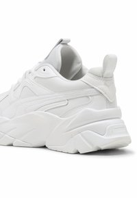 Białe sneakersy z teksturowanego syntetycznego materia�łu, z wyściółką wokół kostki, gumową podeszwą i wyraźną pętelką z tyłu. Charakteryzują się warstwowym wzornictwem i tonacjami stworzonymi przez przeszycia.