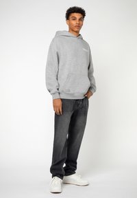 Grijze fleecetrui met een voorzak en geribde manchetten, gecombineerd met donkere jeans en witte sneakers, wat zorgt voor een casual outfit.