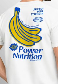 Weißes T-Shirt mit blauer Schrift, die den Satz "Power Nutrition" und einem gelben Bananendesign zeigt, das "Bananengeschmack" und "Beste Geschmacksverbesserung" anzeigt.