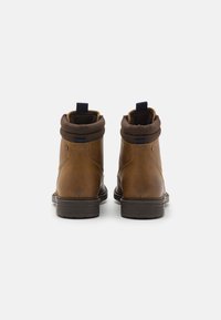 Botas de tobillo de cuero marrón con punta redondeada, collar de textil marrón, lazo en el talón azul y suela de goma texturizada. Vista trasera, sin cordones.