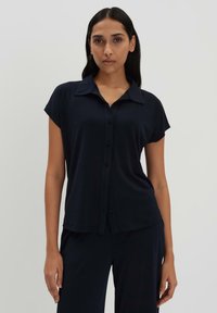 Camicia a maniche corte blu navy in tessuto morbido con colletto a punta e orlo ben ripiegato. Bottoni frontali e vestibilità comoda.