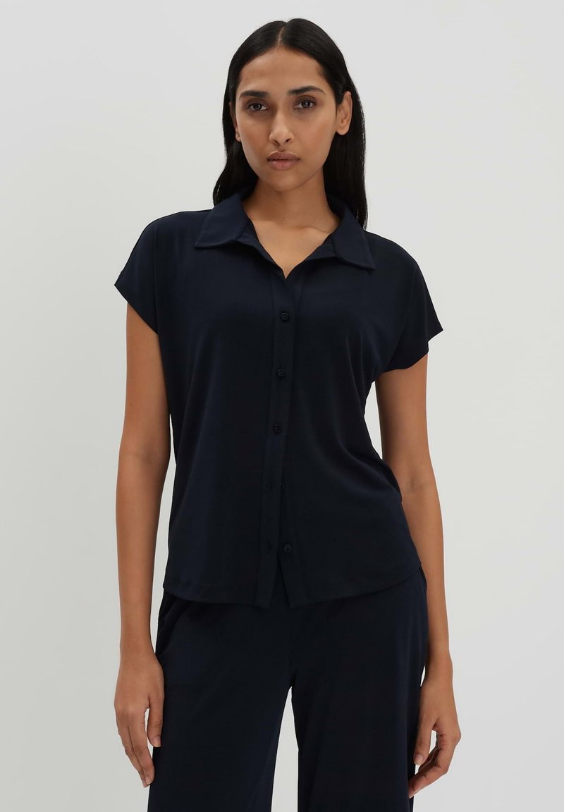 Camicia a maniche corte blu navy in tessuto morbido con colletto a punta e orlo ben ripiegato. Bottoni frontali e vestibilità comoda.