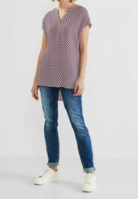 Blusa con scollo a V profondo, maniche corte e un motivo geometrico rosso e bianco. Indossata con jeans arrotolati e sneakers bianche.