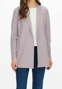 Blazer grigio chiaro con vestibilità rilassata, chiusura a un bottone e rever a punta, abbinato a una camicia bianca e jeans blu. Texture liscia.