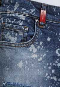 Jeans i denim med en blå tvätt, smakfullt dekorerade med ett stänkmönster, fransade kanter, en frampocket och en metalltagg fästad vid midjan.