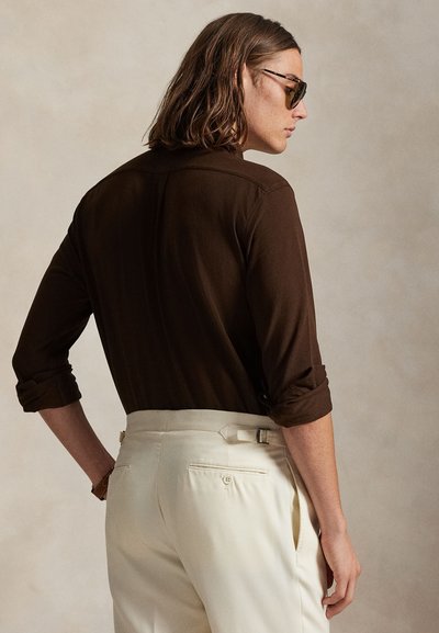 Καφέ μακρυμάνικο πουκάμισο με σηκωμένα μανίκια, συνδυασμένο με κρέμ παντελόνι με θηλιές ζώνης και λεπτομέρειες πίσω τσέπης.