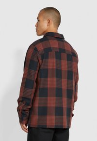Camicia a quadri rossa e blu navy con colletto alla francese, maniche lunghe e una vestibilità rilassata. Presenta un tessuto testurizzato con motivi a rilievo contrastanti.
