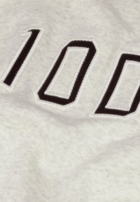 Gros plan sur un tissu blanc avec des chiffres brodés en noir et blanc "100" cousus sur la surface.