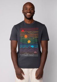 Donkergrijze T-shirt met een meerkleurig geometrisch landschap ontwerp, met lijnen die bergen en zonnen in oranje, rood en blauwe tinten uitbeelden.