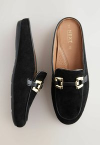 Czarne zamszowe buty typu slip-on z gładkim czarnym skórzanym akcentem i złotymi dekoracyjnymi klamrami. Wnętrze wyposażone w beżową, wyściełaną wkładkę.