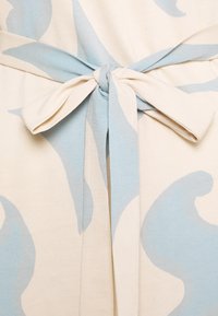 Cremefarbener Stoff mit großen hellblauen Wirbeln; verfügt über einen passenden Krawattengürtel in der Taille. Weiche Textur und lässiges Design.